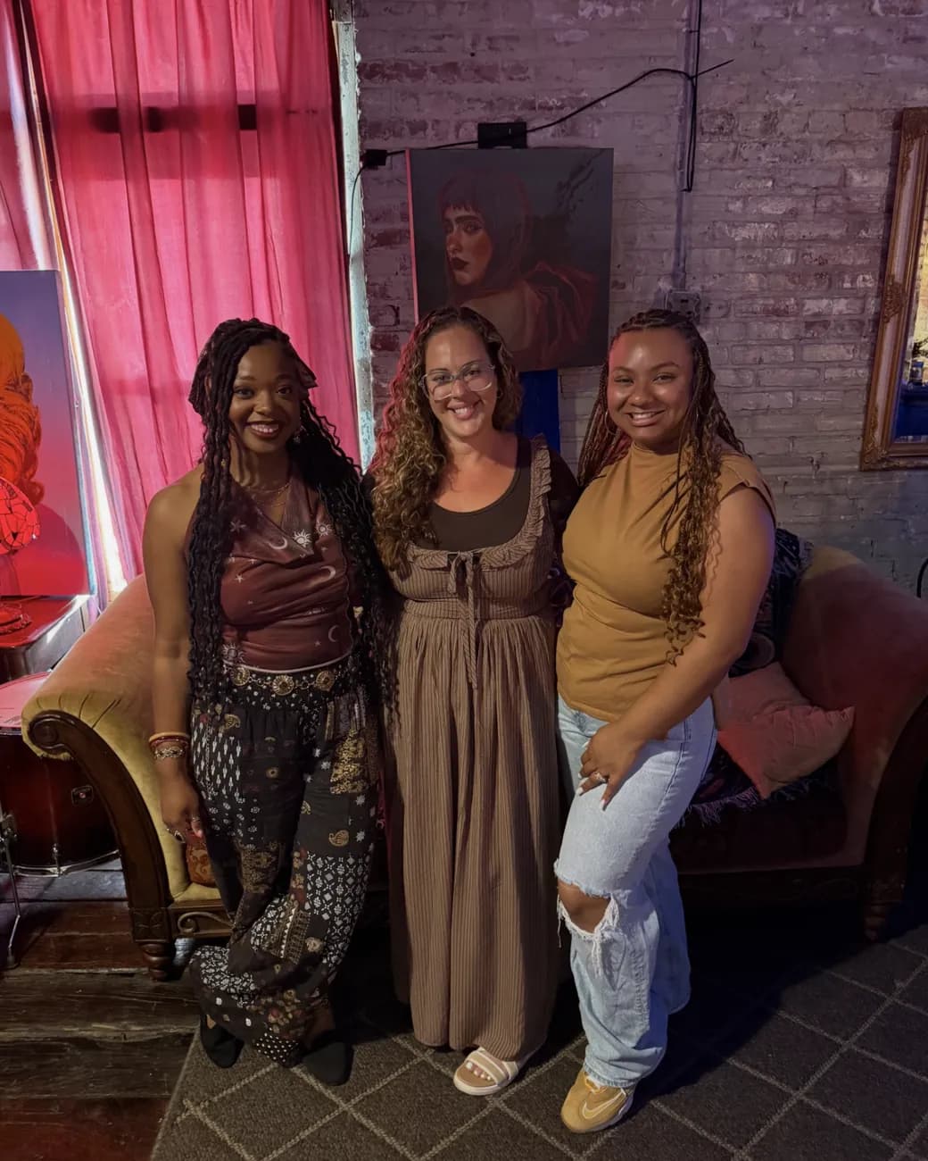 Cristina Vann, smiling in the middle, with two women from one of her shoots in a brick-walled studio.